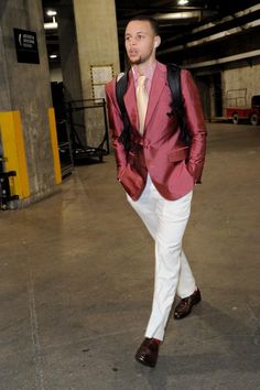 a man in a red jacket and white pants walking through a parking garage with his hands in his pockets