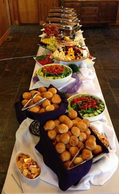 a buffet line with many different types of food on the table, including rolls and salads