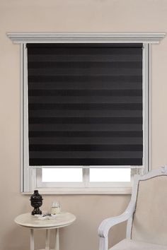 a living room with a white table and chair next to a window covered in black roller shades