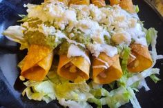 a black plate topped with tortilla shells covered in cheese and lettuce