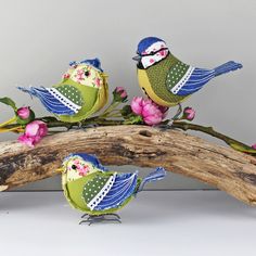 three small birds sitting on top of a branch with flowers in the back and behind them