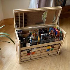 a wooden box filled with lots of different colored pens and pencils on top of a hard wood floor