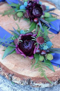 two purple flowers are sitting on a piece of wood with blue ribbon around it and greenery