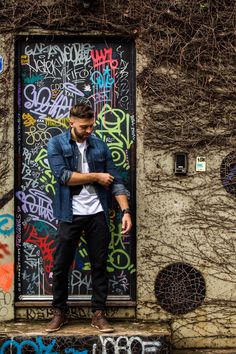 a man standing in front of a graffiti covered wall with his hands on his hips