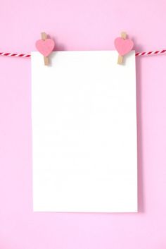 two hearts on clothes pins attached to a white sheet of paper against a pink background