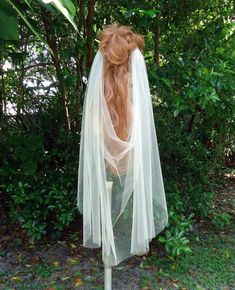 the back of a woman's head wearing a white veil in front of trees