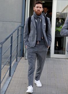 a man with a beard wearing a gray suit and white sneakers walking down the street