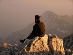 a man sitting on top of a large rock next to a mountain covered in fog