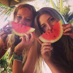 two beautiful young women holding slices of watermelon in front of their faces while standing next to each other