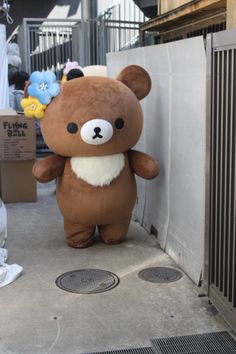 a large brown teddy bear standing next to a white wall and some metal grates