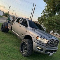 a large gray truck parked on top of a lush green field next to a tree