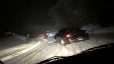 two cars driving down a snowy road at night