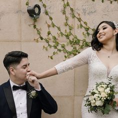 a bride and groom standing next to each other in front of a wall with vines