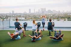 a group of people doing exercises on top of a roof with city in the background