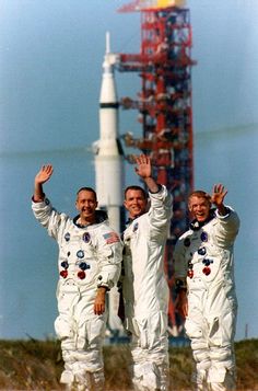 three men in white spacesuits waving at the camera