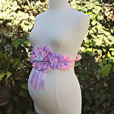 a pregnant woman's torso wearing a pink and purple flower sash