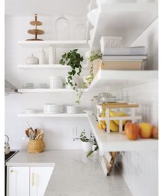 a kitchen with white walls and shelves filled with dishes, fruit and other things on the counter