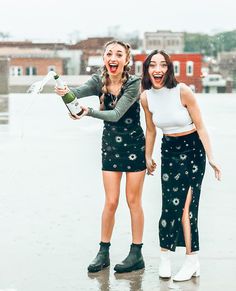 two girls standing in the rain with their arms around each other and one holding a bottle