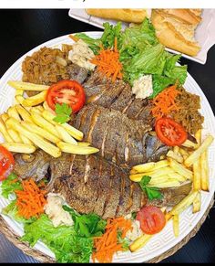 a plate with fish, french fries and tomatoes on it next to some breads