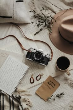 an old camera, hat, book and other items on a bed with white sheets