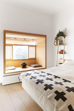 a bed sitting under a window next to a wooden shelf filled with pots and vases