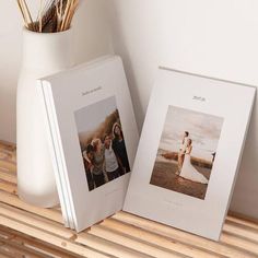 two white frames sitting next to each other on a wooden shelf in front of a vase