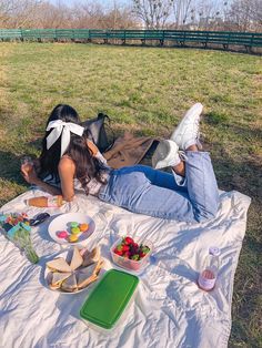 a woman laying on top of a white blanket next to a picnic table filled with food