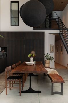 a dining room table with chairs and a bench in front of some hanging lights above it