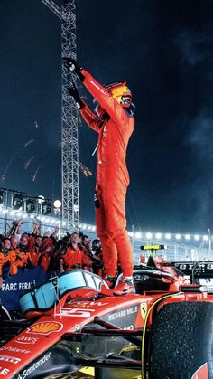 a man standing on top of a red race car in front of a large crowd