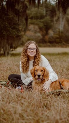 a woman sitting in the middle of a field with her dog and looking at the camera