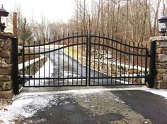 an iron gate is open to the driveway and street with snow on the ground in front of it