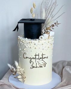 a graduation cake decorated with pearls, feathers and a black topper on a white plate