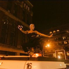 a woman standing on top of a white car in the middle of a city at night