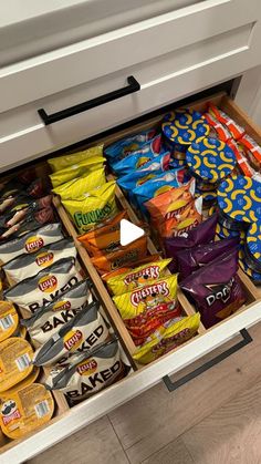 an open drawer in a kitchen filled with chips and candy bars on the bottom shelf