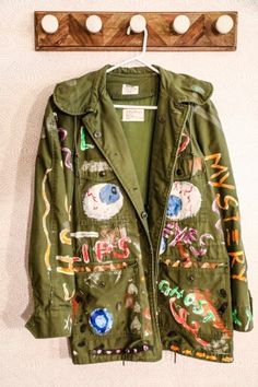 an army green jacket hanging on a wall next to a coat rack with buttons and magnets