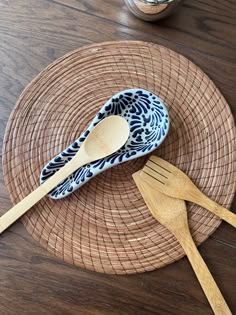 two wooden utensils sitting on top of a woven plate next to a jar