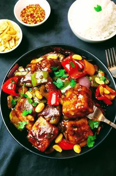 a black plate topped with meat and veggies next to bowls of rice on a table