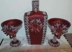 a red vase and two crystal goblets sitting on top of a white cloth