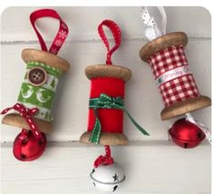 three spooled christmas ornaments hanging from the side of a white wooden wall with red and green ribbons on them