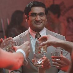 a man in a suit and tie is holding some wine glasses with other people around him