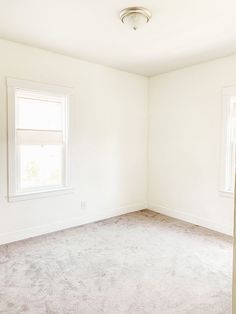 an empty room with two windows and carpet