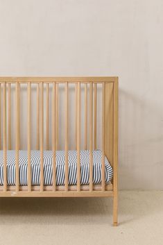 a small wooden crib with blue and white striped sheets on the bottom, in front of a beige wall