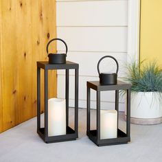 two black lanterns sitting next to each other on the ground near a plant and door