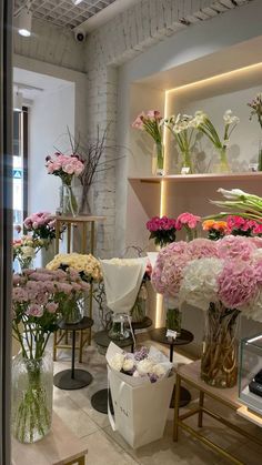 a room filled with lots of different types of flowers in vases on tables next to shelves