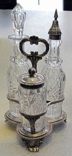 three glass bottles sitting on top of a silver tray with an ornate handle and lid