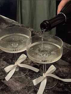 someone pouring wine into two glasses on top of a marble counter with white ribbons around the rims