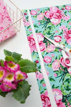 a pair of scissors sitting on top of a table next to pink flowers and green leaves