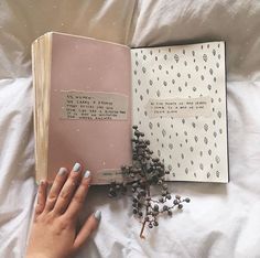 a woman's hand holding an open book on top of a bed with white sheets