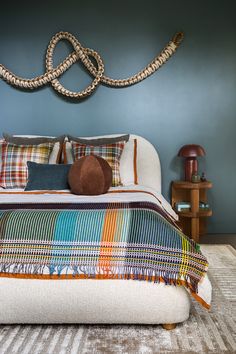 a bedroom with blue walls and plaid bedding on the bottom floor, along with a rope sculpture above the bed