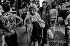 black and white photograph of people walking on the sidewalk in front of a bus stop